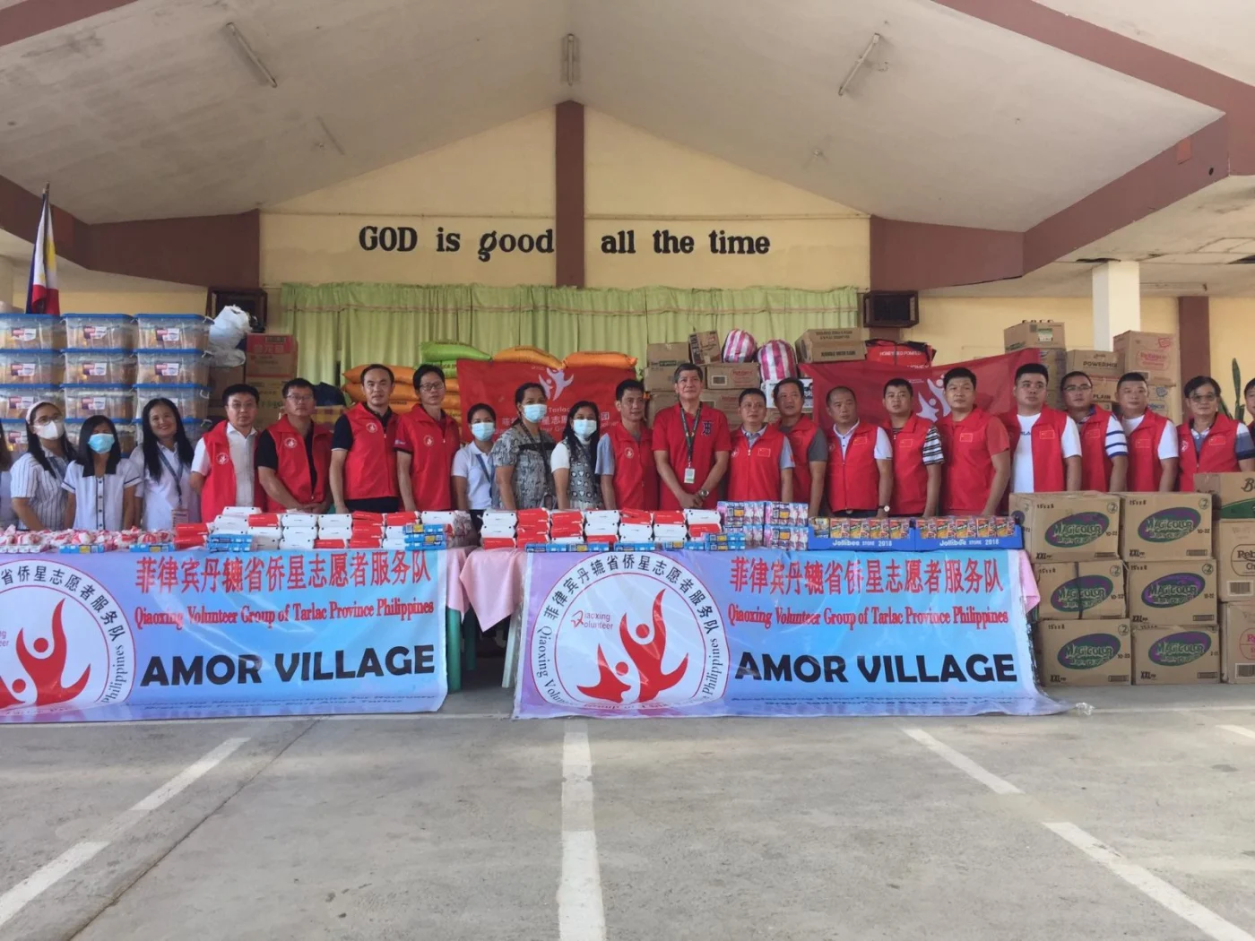 Community supporters stand behind supplies and AMOR Village banners.
