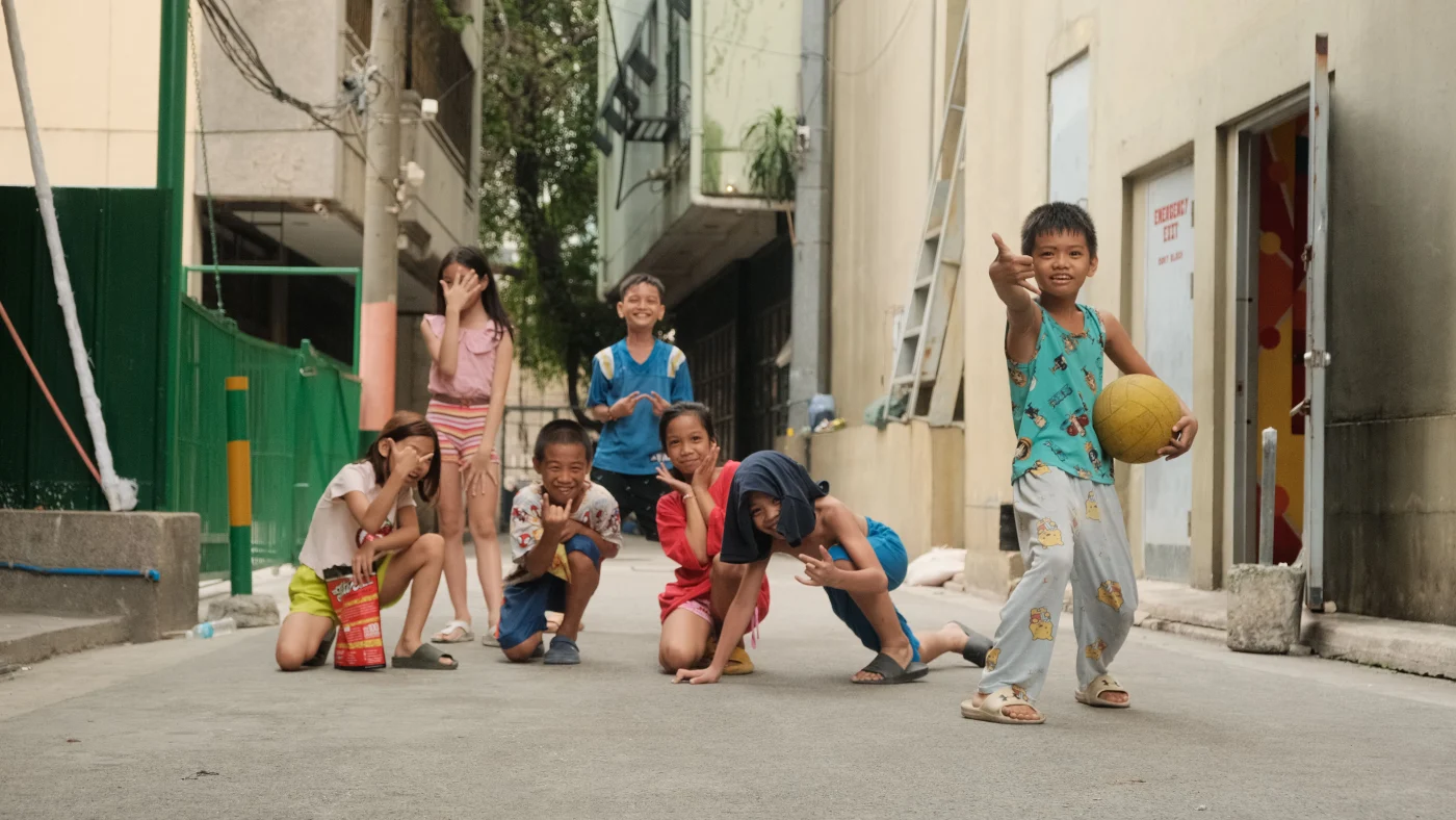 Children playing together on a street in Manila, including a child holding a yellow ball.